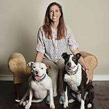 dr. rachel horsey employyee photo sitting indoors with two dogs all smiling into camera